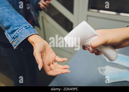 Misurazione della temperatura mediante termometro elettronico a infrarossi della mano di una donna all'ingresso di un supermercato. Pandemia di coronavirus. Stile di vita. Foto Stock