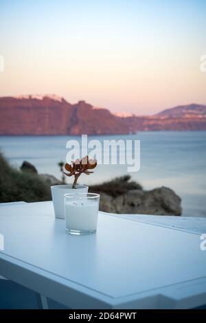 Decorazione di candela e piante su un tavolo bianco. Oia, isola di Santorini, grecia. Splendidi colori del tramonto sulla caldera. Formato verticale Foto Stock