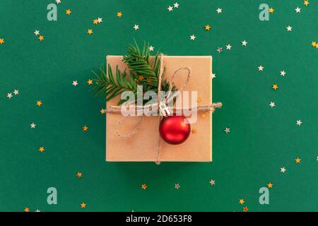 Regalo di Natale in scatola con pallina rossa e confetti su sfondo verde. Vista dall'alto, disposizione piatta. Foto Stock