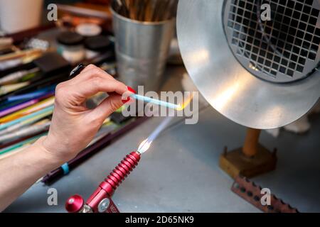 L'artista riscalda il vetro con un bruciatore a gas. Il processo di fabbricazione dei monili di vetro. Le mani del maestro si avvicinano Foto Stock