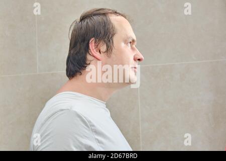 Ritratto di un uomo in una t-shirt bianca, primo piano. Volto di un uomo di 35-40 anni di profilo su sfondo beige Foto Stock