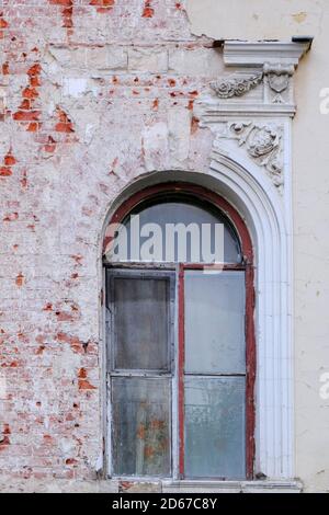 Frammento di facciata e finestra ad arco con rovina stucco di un vecchio edificio abbandonato. Foto Stock