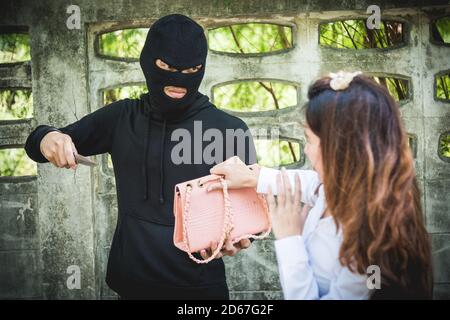Il rapinatore sta derubando la femmina con un coltello, puntando il coltello verso il viso Foto Stock