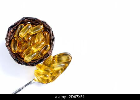 Primo piano di capsule di olio di pesce in un cucchiaio e cestino su sfondo bianco. Omega 3 capsule - vitamine naturali. Foto Stock