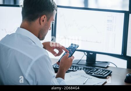 Giovane uomo d'affari in abiti formali è in ufficio con schermi multipli. Concezione dello scambio e del denaro Foto Stock