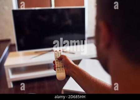 La vista posteriore di MAN tiene il telecomando in mano e. Accendere il televisore Foto Stock