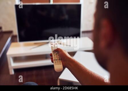 La vista posteriore di MAN tiene il telecomando in mano e. Accendere il televisore Foto Stock