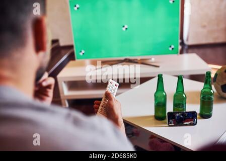 La vista posteriore di MAN tiene il telecomando in mano e. Accendere il televisore Foto Stock