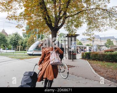 Strasburgo, Francia - 10 ottobre 2020: Vista posteriore di una donna che corre per prendere il tram per la stazione del tram indossare maschera protettiva durante la pandemia covid 109 Foto Stock