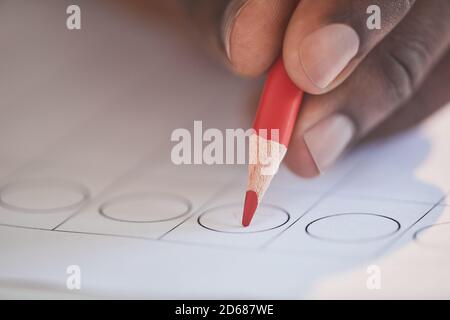 Primo piano di uomo che mette il segno di spunta sul voto con rosso matita durante la votazione Foto Stock