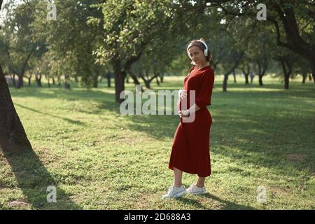 Donna incinta che ascolta una musica al parco. Foto Stock