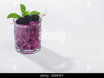 Bicchiere di rinfrescante cocktail estivo con mora, ghiaccio e menta su sfondo bianco. Miscela di bevande analcoliche e alcol. Luce dura con ombre profonde. Foto Stock