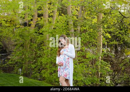 Giovane donna incinta che cammina nella foresta e indossa abiti. Foto Stock