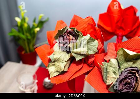Una rosa rossa appassita con un grande nastro rosso in piedi su un tavolo in un vaso. Foto Stock