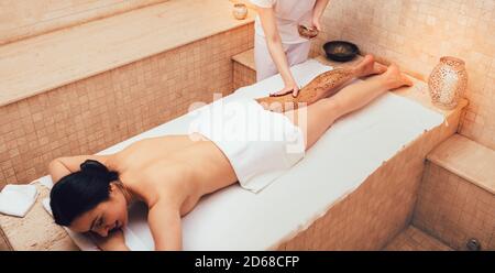 Spa salon operaio che applica scrub sulle gambe di un cliente salone di bellezza. Esfoliare la pelle più vecchia dei piedi con uno scrub corpo. Procedura di spellatura della brunetta Foto Stock