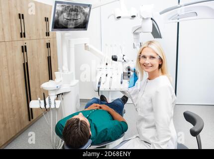 Ritratto di una bella dentista femminile in uniforme medica mentre trattamento di un paziente in uno studio odontoiatrico Foto Stock
