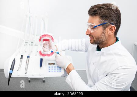 Dentista esperto che mostra il giusto senso che spazzolando i denti nel suo studio dentistico. Una corretta pulizia dei denti è la chiave del successo di un bel sorriso. Foto Stock