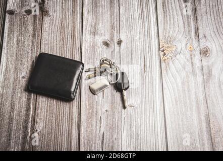 Un portafoglio e una serie di chiavi posate su un tavolo o scrivania rustici in legno Foto Stock