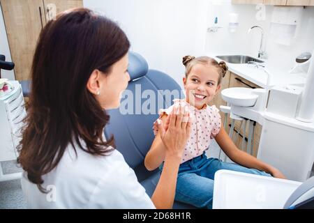 Trattamento dei denti per bambini. Sorridente bambina dà cinque al dentista, lei seduta nella sedia del dentista. I miei denti sono sani Foto Stock