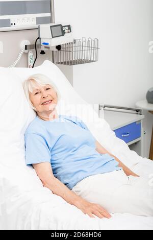 La donna anziana si trova in un letto d'ospedale di umore positivo perché ha recuperato dalla sua malattia ed è completamente sana. Medicina moderna accessibile Foto Stock