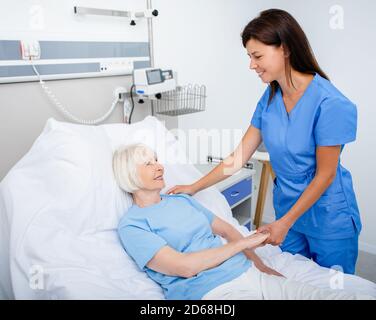 Infermiera cordiale che si prende cura di una donna anziana in una stanza dell'ospedale. Trattamento di pazienti anziani Foto Stock
