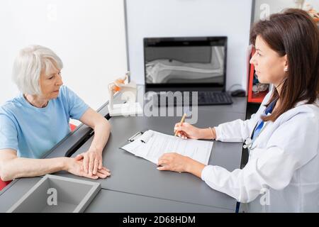 La donna anziana parla al medico osteopatico del dolore alle articolazioni e del tremore della mano. Diagnosi e trattamento dolore articolare nelle persone anziane Foto Stock