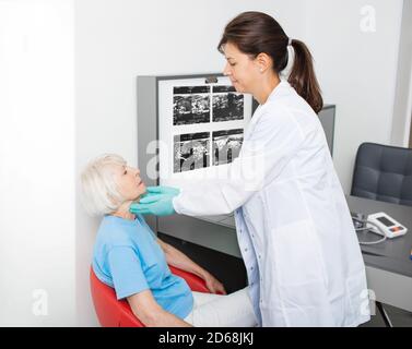 medico che controlla la ghiandola tiroidea di una donna anziana. Diagnosi di malattie della tiroide. Trattamento del sistema endocrino Foto Stock