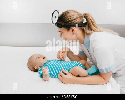 Il pediatra sorridente comunica e gioca con il bambino in ospedale. il medico esamina il neonato di 3 mesi Foto Stock