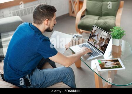 Uomo che lavora da casa, utilizzando dispositivi, concetto di ufficio remoto. Giovane uomo d'affari, manager che fa compiti con il laptop, ha conferenza online. Coronavirus, COVID-19 prevenzione della diffusione del virus. Foto Stock