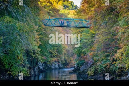 I visitatori ammirano la vista dal ponte pedonale con i colori autunnali sugli alberi che circondano il fiume Garry a Garry Bridge vicino a Killiecrankie, Scozia, Regno Unito Foto Stock