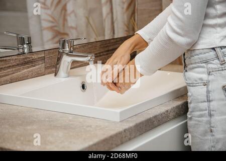 Donna lava le mani sotto un miscelatore dell'acqua usando acqua e sapone Foto Stock