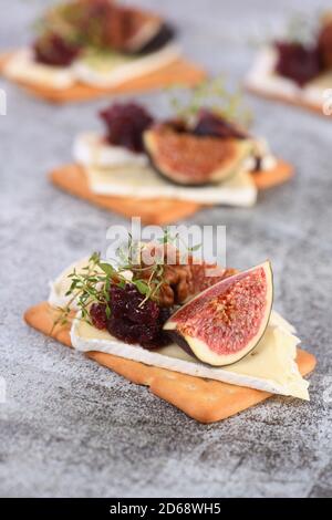 Cracker con una fetta di camembert, marmellata, fichi e noci. Un'ottima idea di spuntino per una vacanza, un picnic o una festa. Foto Stock