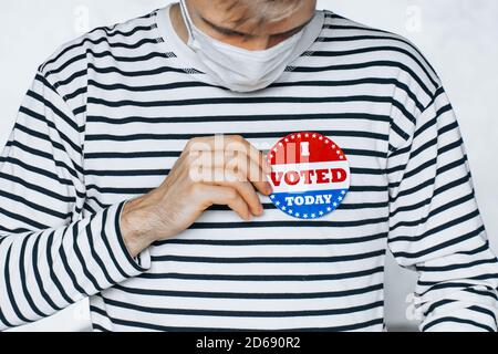 Giovane uomo in faccia maschera medica indossando sulla camicia ho VOTATO OGGI pin. Giorno di elezione sulla pandemia coronavirus. Elezioni di novembre negli Stati Uniti 2020. Foto Stock