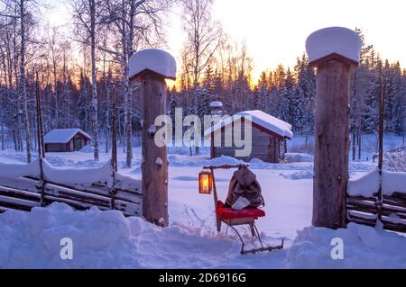 Una slitta con una lanterna e uno zaino davanti di un cottage tradizionale in paesaggio invernale Foto Stock