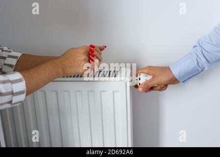 Mano maschio regolazione della manopola del radiatore di riscaldamento. Una mano che regola la temperatura nel radiatore e le mani della donna sfregate con freddo. Mani calde Foto Stock