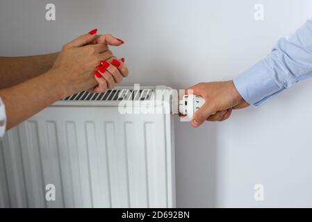 Mano maschio regolazione della manopola del radiatore di riscaldamento. Una mano che regola la temperatura nel radiatore e le mani della donna sfregate con freddo. Mani calde Foto Stock