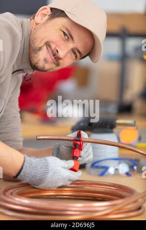 un uomo sorridente taglia il tubo di rame con l'ausilio di un attrezzo speciale Foto Stock