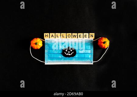 Zucche di Halloween, maschera medica protettiva e foglie di acero giallo su sfondo nero, pipistrelli di carta nera. L'iscrizione HALLOWEEN il Foto Stock