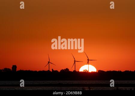 Generatori di vento silhouette fattoria sull'alba rosso arancio vibrante cielo e grande sorgere sole. Turbine energetiche industria sostenibile Foto Stock