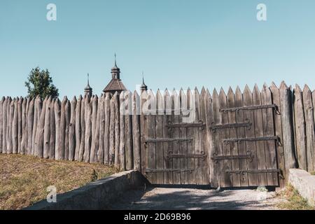 Recinzione medievale in legno e porte al sich Zaporozhian, facciata forte con chiesa in lontananza, stato di cosacchi sull'isola Khortytsia, ucraino culturale h Foto Stock