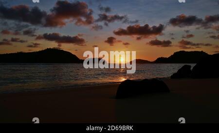 Tramonto mozzafiato sulla spiaggia tropicale vicino a Port Launay, Mahe, Seychelles con sole di colore arancione tra le sagome di due isole riflesse in acqua. Foto Stock