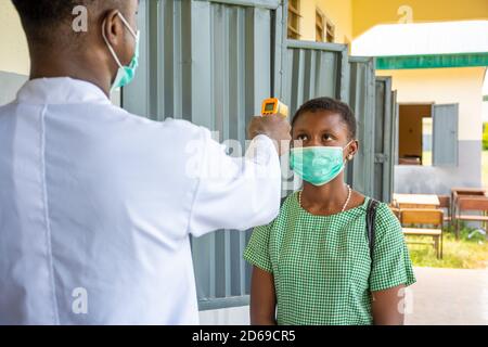 insegnante in una scuola africana che controlla la temperatura corporea del bambino prima entra in classe Foto Stock