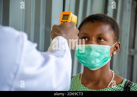 primo piano di un insegnante in una scuola africana che controlla la temperatura corporea dell'allievo prima di entrare in classe Foto Stock