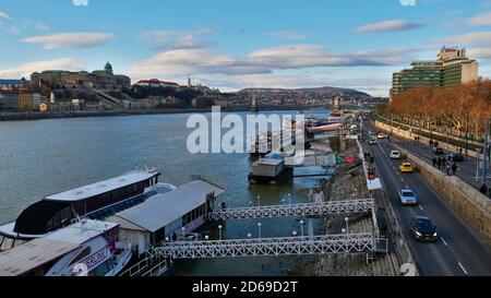 Budapest, Ungheria - 12/31/2018: Vista sul Danubio con attracco per le navi passeggeri, strada trafficata e skyline con il famoso storico Castello di Buda. Foto Stock