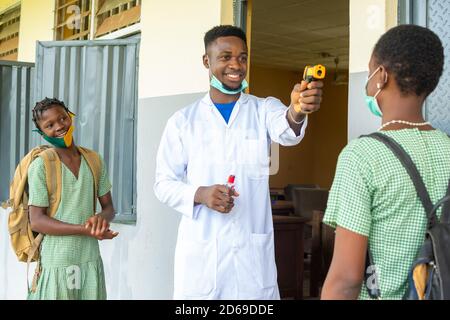 insegnante in una scuola africana che controlla la temperatura del bambino della scuola prima entra in classe Foto Stock