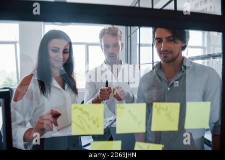 Gli adesivi gialli sono sul vetro. Giovani uomini d'affari in abiti formali che lavorano in ufficio Foto Stock
