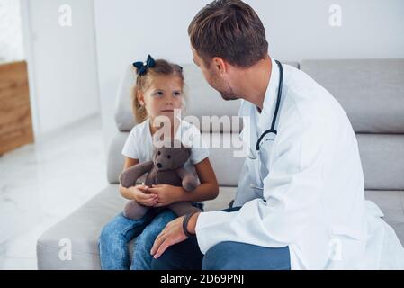 Medico maschile in uniforme bianca siede in clinica con bambina Foto Stock