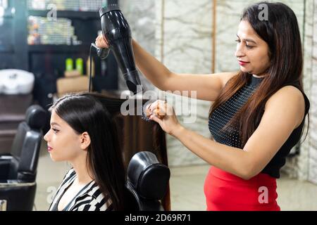 Un parrucchiere fornisce servizi di styling dei capelli ad una giovane donna indiana graziosa, bella donna ottiene i suoi capelli fatti ad un salone, fuoco selettivo. Foto Stock