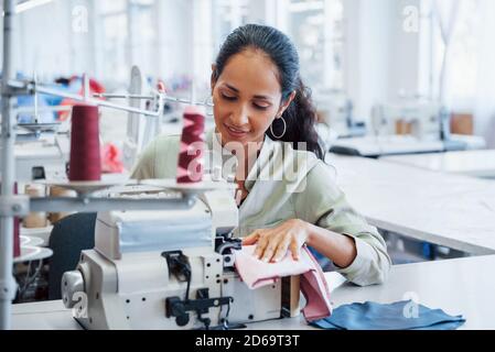 Donna di dressmaaker cucina i vestiti sulla macchina da cucire in fabbrica Foto Stock