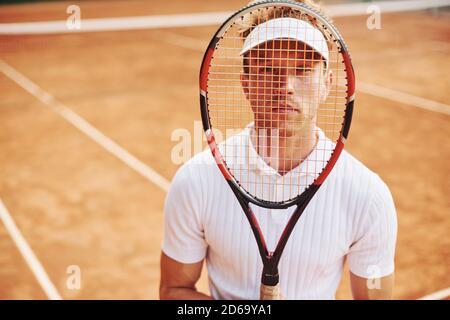 Tiene la racchetta nelle mani. Il giovane tennista in abiti sportivi si trova sul campo all'aperto Foto Stock